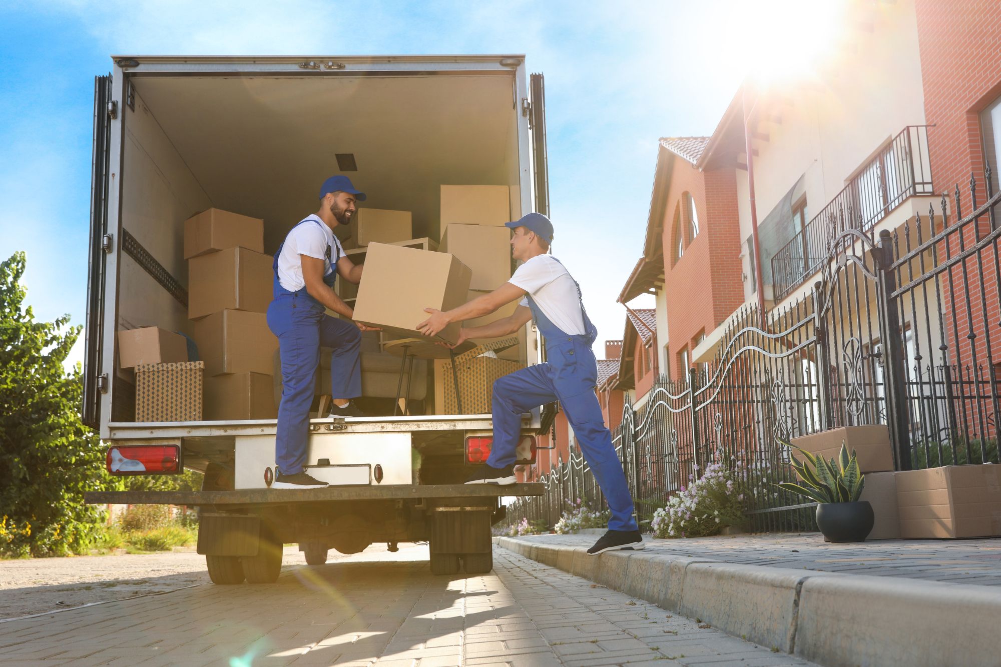 Two men in blue overalls are seen loading boxes into a moving truck for an outdoor junk removal service in Columbia, SC.