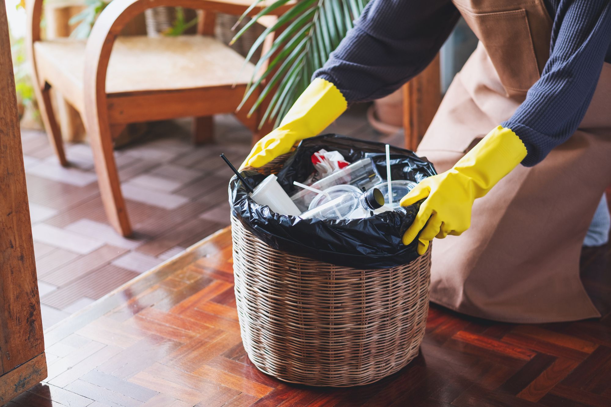 A woman in an apron and rubber gloves holds a trash basket, illustrating a clean-out service in Columbia, SC.